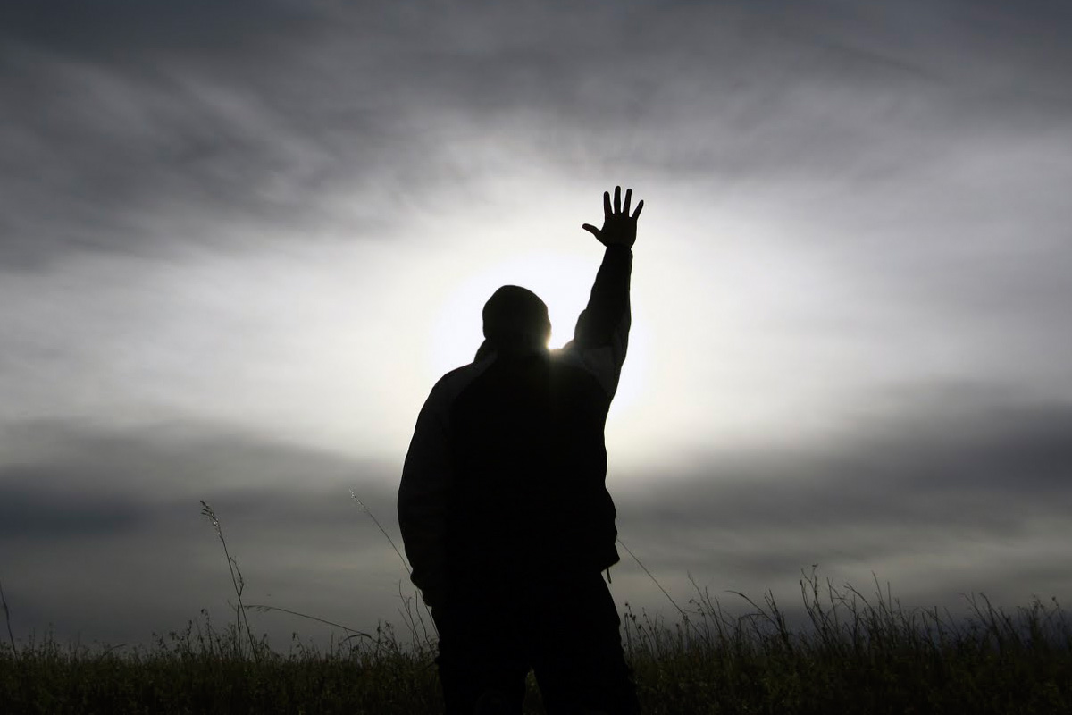 a person standing outside with their hand rasied to the sky